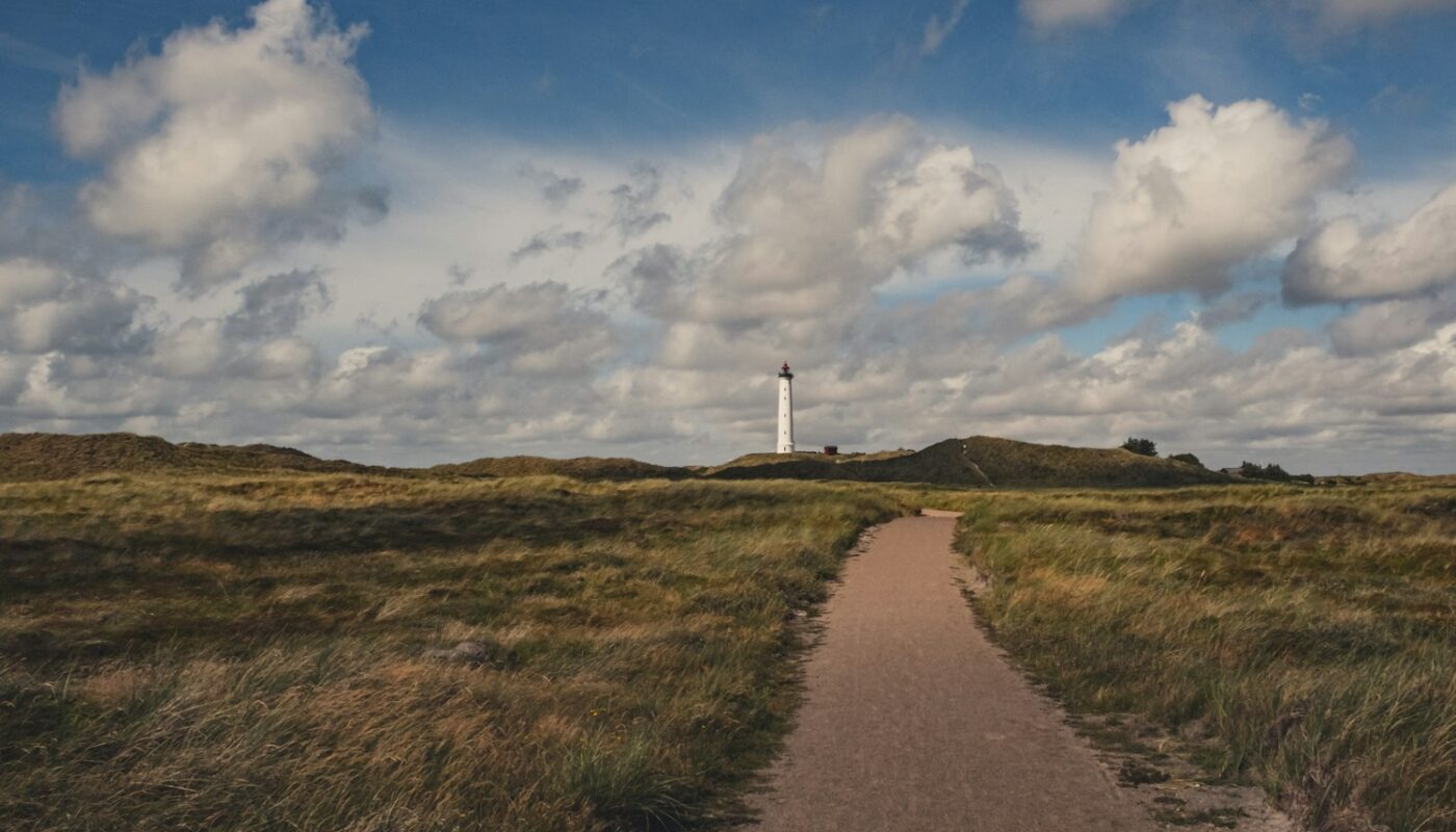 white lighthouse on green grass field under blue and white cloudy sky during daytime