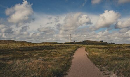 white lighthouse on green grass field under blue and white cloudy sky during daytime